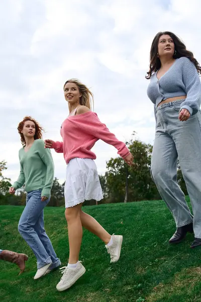 Trois amis à la mode marchent en toute confiance, profitant des couleurs vives du printemps dans un parc. — Photo de stock