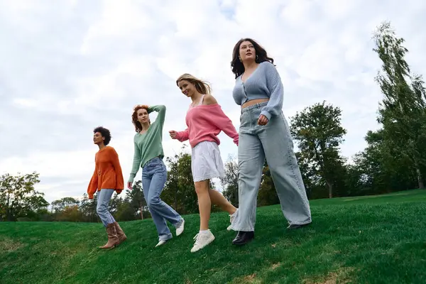Quatre femmes élégantes se promènent ensemble, mettant en valeur leur mode unique contre un paysage vert. — Photo de stock