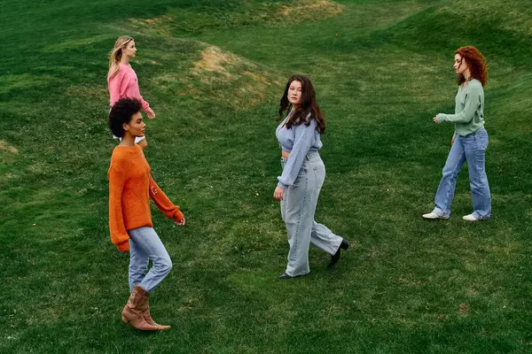 Cuatro mujeres de moda pasean con confianza por un exuberante parque verde, abrazando la belleza de los manantiales. - foto de stock