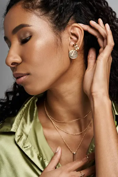 A beautiful African American woman elegantly adjusts her jewellery while dressed in stylish attire. — Stock Photo