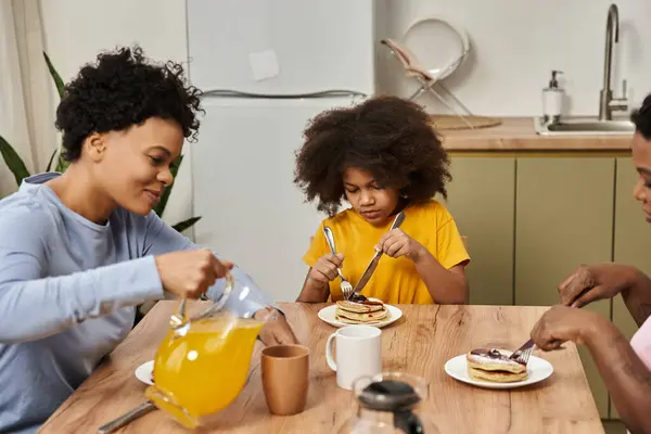 Three family members enjoy a cozy breakfast of pancakes and juice in their warm kitchen. — Stock Photo