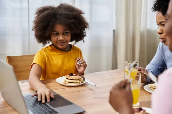 Una giovane ragazza sorride mentre mangia frittelle a un accogliente tavolo per la colazione con i suoi genitori nelle vicinanze. — Foto stock