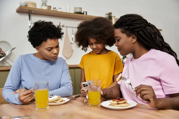 Three family members savoring breakfast and bonding over shared moments in their cozy kitchen. — Stock Photo