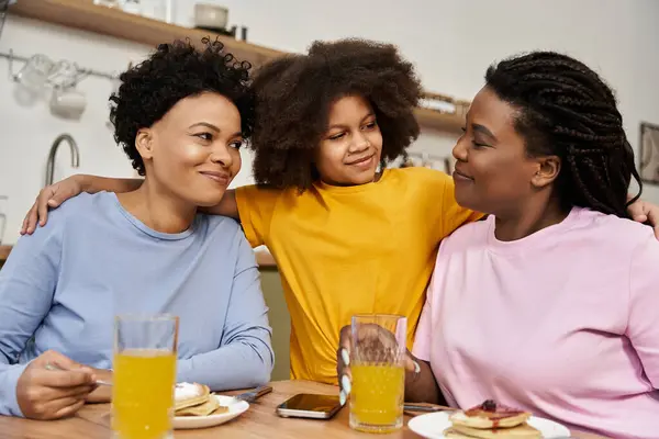 Três membros da família compartilham sorrisos e risos na mesa do café da manhã, saboreando panquecas juntos.. — Fotografia de Stock