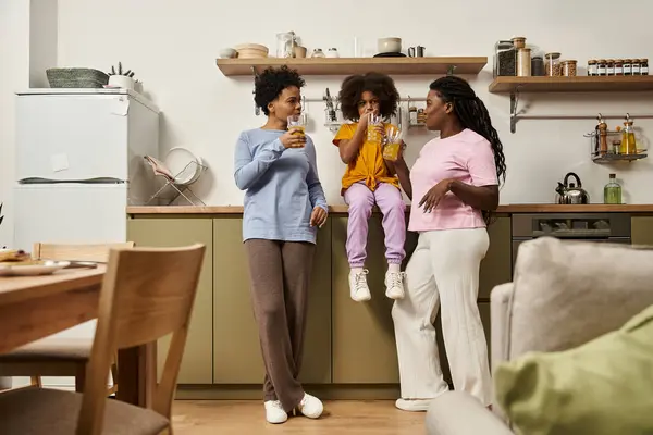 Three family members enjoy playful moments in their bright kitchen while sipping on cold drinks. — Stock Photo