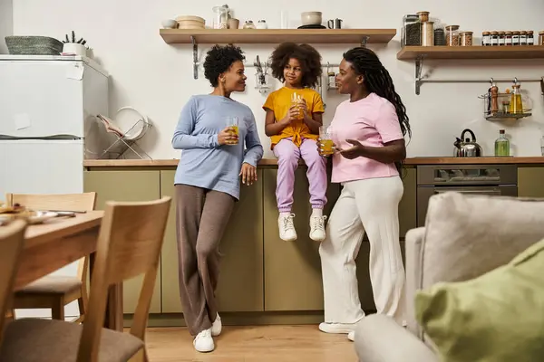 Three family members share laughter and drinks, enjoying quality time in their inviting kitchen. — Stock Photo