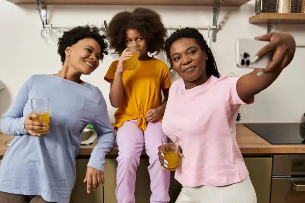 Three family members share laughter and drinks in a cozy kitchen, celebrating their bond together. — Stock Photo