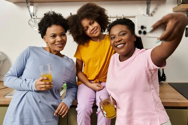 Two mothers and their daughter smile and share a fun moment while taking a selfie in the kitchen. — Stock Photo