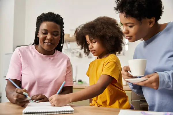Three family members share joyful moments while drawing and sipping tea in their inviting kitchen. — Stock Photo