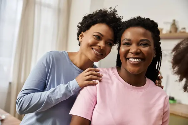 Two smiling mothers share a warm embrace with their daughter nearby in a cozy living space. — Stock Photo