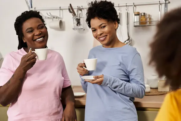Two women share a warm moment together with their daughter while enjoying tea in their cozy kitchen. — Stock Photo