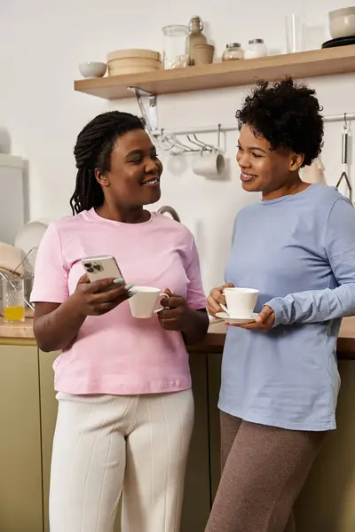 Two women enjoy a warm cup of tea while connecting and sharing laughter in their kitchen. — Stock Photo