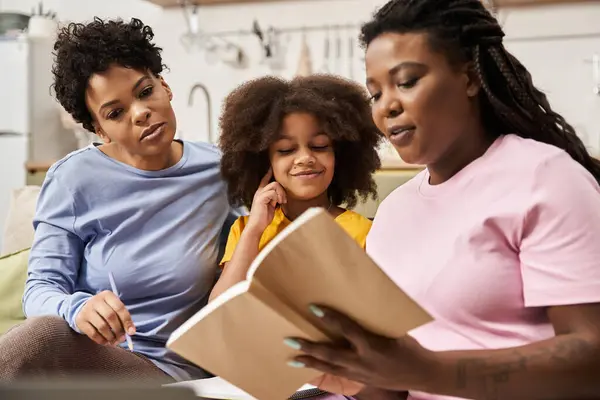 Two mothers and their daughter enjoy reading a book together in a cozy living room. — Stock Photo