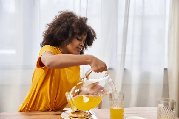 Girl enjoys a cheerful moment pouring orange juice during breakfast at home. — Stock Photo