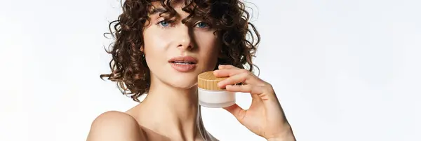 Une jeune femme aux cheveux bouclés partage ses secrets de beauté tout en tenant un pot de soins de la peau. — Photo de stock
