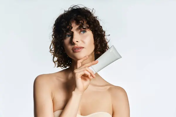 A curly haired woman holds a skincare product, radiating natural beauty and grace. — Stock Photo