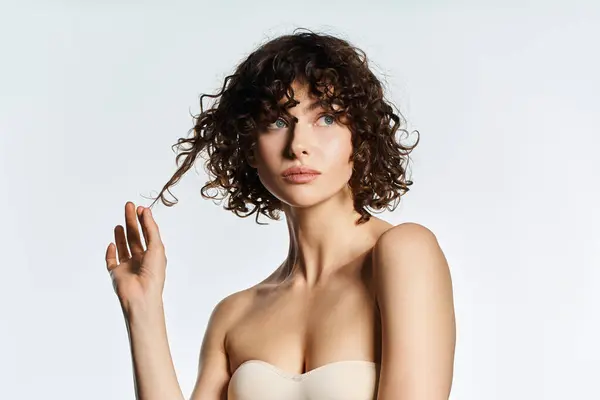 A beautiful young woman with curly hair gently touches her locks, exuding elegance and charm. — Stock Photo