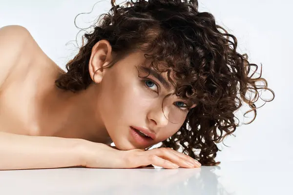Young woman showcases her stunning features with soft curls while relaxing on a smooth surface. — Stock Photo