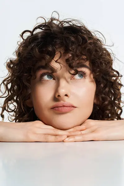 A lovely young woman with beautiful curls rests her chin on her hands, deep in thought. — Stock Photo
