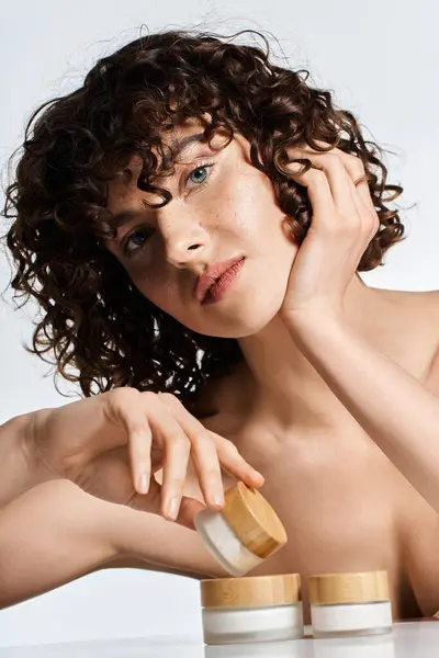 A young woman with curly hair engages with skin care jars, highlighting her natural beauty. — Stock Photo