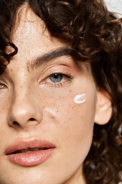 A young woman glows effortlessly with cream on her cheek, showcasing her beauty. — Stock Photo