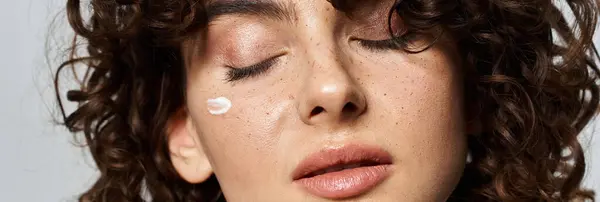 A young woman enjoys a serene moment, applying nourishing cream on her radiant face. — Stock Photo