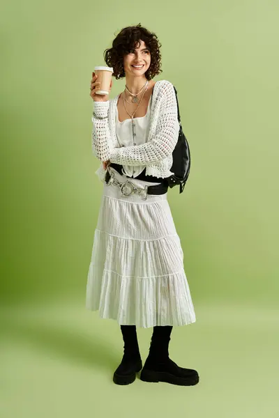 A beautiful young woman holds a warm drink, showcasing her fashion sense with confidence. — Stock Photo