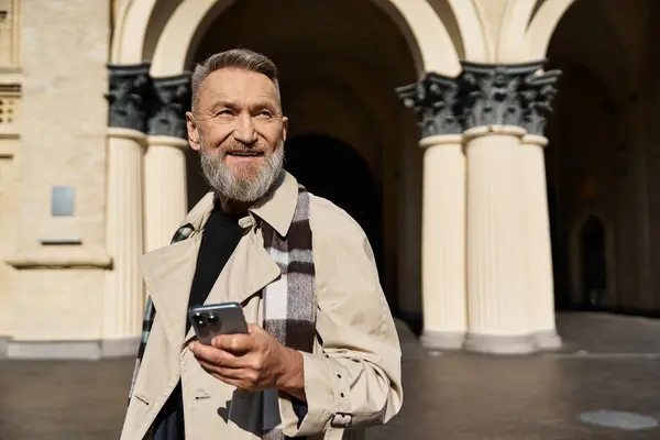 A fashionable senior man strolls through the city, in trendy attire and holding a smartphone. — Stock Photo