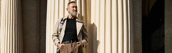 Walking through the vibrant city, a stylish senior man stands confidently against tall columns. — Stock Photo
