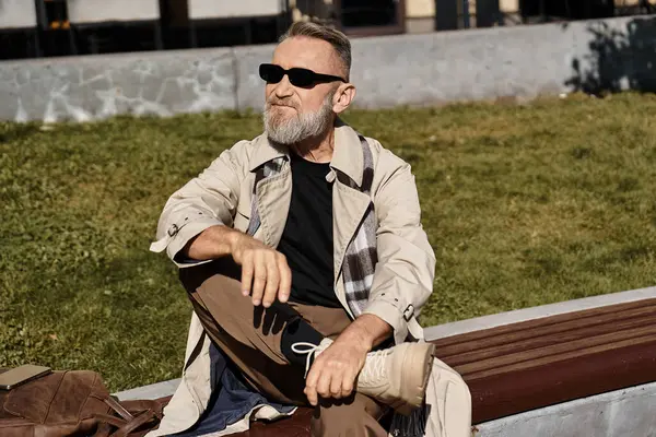 An elegantly dressed senior man sits on park bench, embracing leisure in a city environment. — Stock Photo