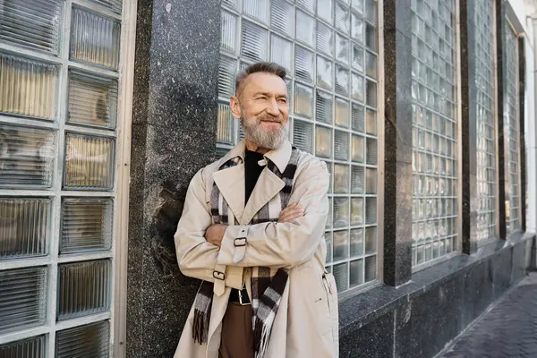 Un uomo anziano si trova con fiducia contro un edificio moderno, in abiti alla moda con una sciarpa alla moda. — Foto stock