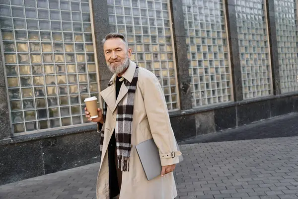 A senior man walks confidently through an urban setting, sipping coffee from a disposable cup. — Stock Photo