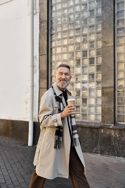 A dapper senior man enjoys a leisurely walk in the city while holding a coffee cup. — Stock Photo