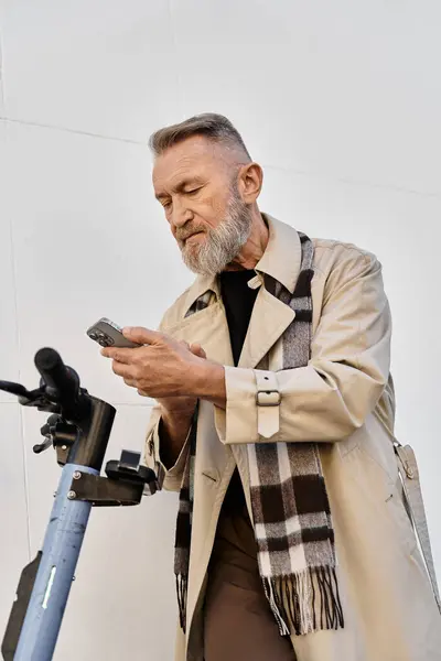 Con un trench chic e una sciarpa alla moda, un bell'uomo anziano si concentra sul suo smartphone. — Foto stock