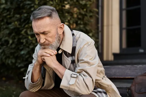 A fashionable senior man sits on a wooden bench, deep in thought amid a contemporary cityscape. — Stock Photo