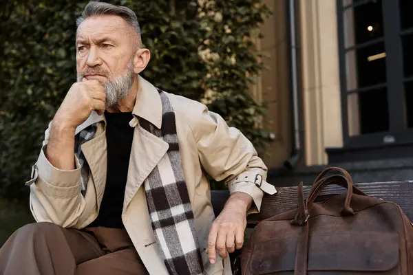A fashionable senior man enjoys some quiet time on a city bench, wearing a chic outfit. — Stock Photo