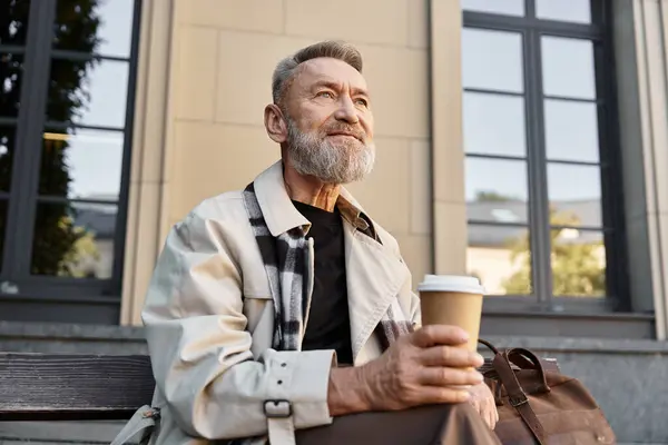 Ein älterer Herr sitzt auf einer Bank, nippt am Kaffee und genießt die Sonne in einem pulsierenden Stadtbild.. — Stockfoto