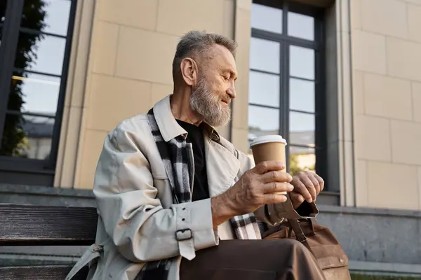 Ein modischer Senior sitzt gemütlich auf einer Parkbank und genießt seinen Kaffee. — Stockfoto