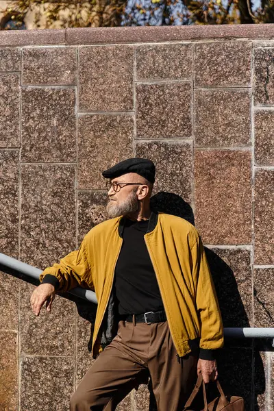 A handsome senior man showcases his fashionable flair in a trendy outfit, leaning against a wall. — Stock Photo