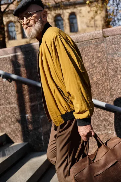 A fashionable senior man walks confidently along city steps, dressed in a trendy outfit. — Stock Photo