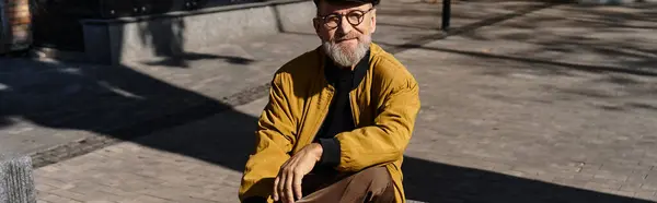 In a fashionable ensemble, a senior man exudes charm as he sits casually on a stone bench. — Stock Photo