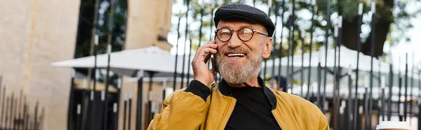 A stylish senior man dressed in fashionable attire engages in a lively phone conversation. — Stock Photo