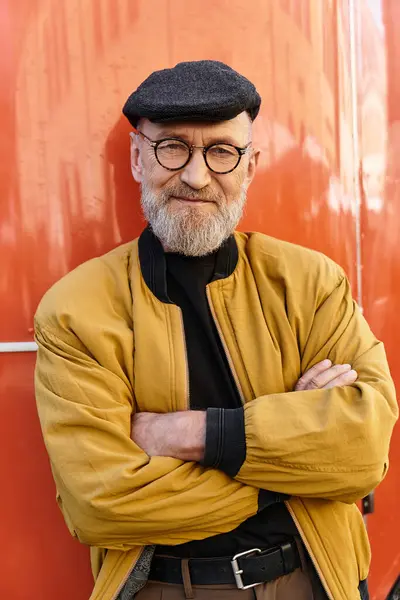Dapper senior man stands with arms crossed, exuding charm in an eye catching jacket and trendy cap. — Stock Photo