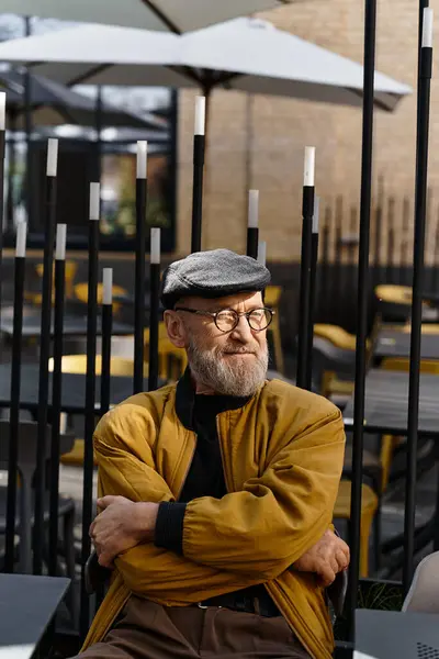 A handsome senior man sits casually with arms crossed in a trendy urban cafe. — Stock Photo