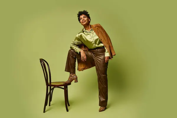 Mujer afroamericana con estilo posa con confianza en una silla con un atuendo elegante. - foto de stock