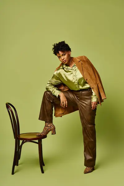 A fashionable african american woman displays trendy style while elegantly perched on a chair. — Stock Photo
