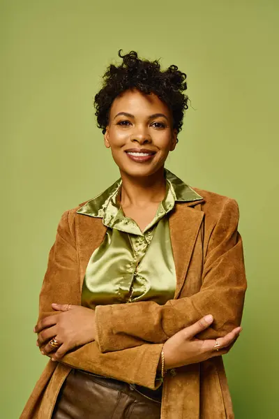 A beautiful woman in a chic outfit smiles confidently with arms crossed against a green backdrop. — Stock Photo