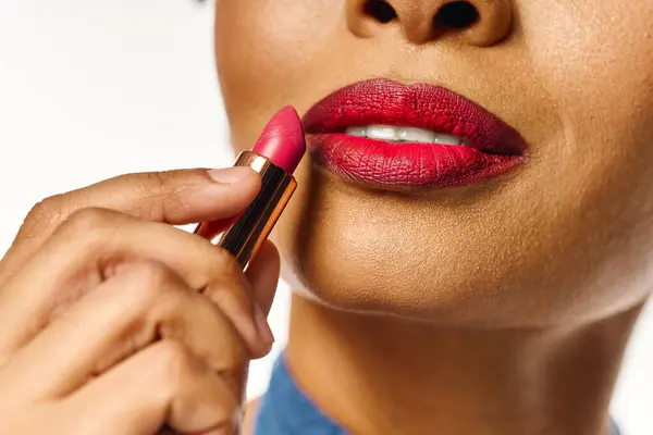 Chic african american woman enhances her beauty with vibrant lipstick in a modern, bright setting. — Stock Photo