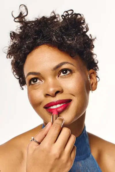 A stylish african american woman enhances her beauty with vibrant lipstick in a chic environment. — Stock Photo