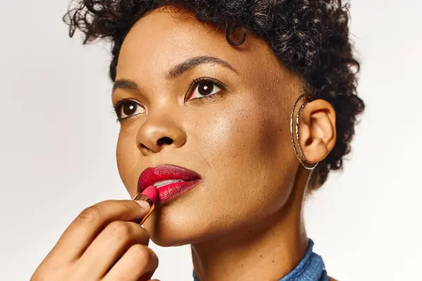 A beautiful african american woman enhances her look with vibrant lipstick in a chic environment. — Stock Photo